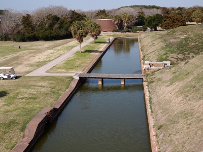 [Long water channel split in half with a wooden series of planks supported by two pillars in the water.]